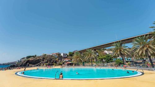 a large swimming pool on a beach with palm trees at Casa do Mundo Madeira in Gaula