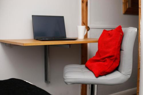 almohada roja sentada en una silla junto a un escritorio con ordenador portátil en Harmony Haven - Amity Suite en Nottingham