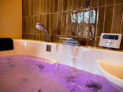 une baignoire remplie d'eau violette à côté d'un lavabo dans l'établissement Love Room Suite Bali - Auray en Bretagne, à Brech