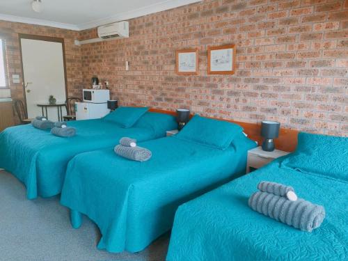a room with three blue beds and a brick wall at Hills of Gold Motel at Nundle in Nundle
