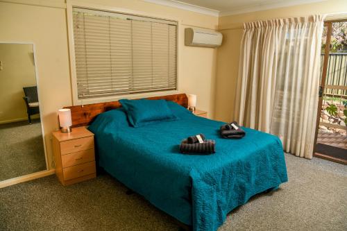 a bedroom with a bed with a blue blanket and a window at Hills of Gold Motel at Nundle in Nundle
