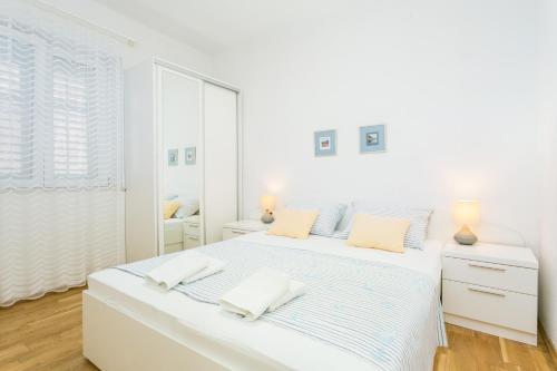 a white bedroom with a large bed with two pillows at Apartments by the sea Podgora, Makarska - 6846 in Podgora