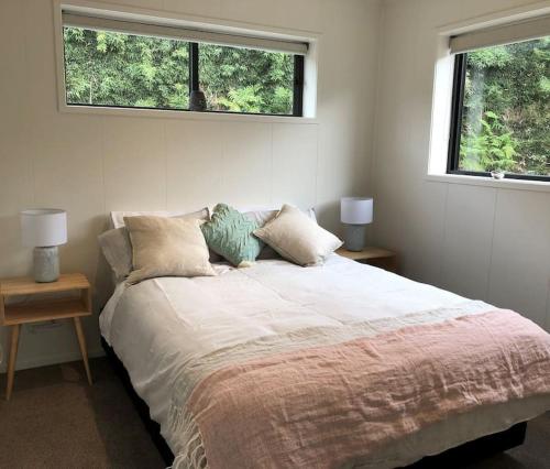 a bedroom with a large bed with two windows at Brightside Cosy Farmstay in Papamoa