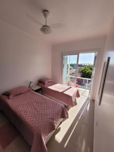 two beds in a room with a window at Apto 2 quartos - 250 m da praia de Atlântida in Xangri-lá