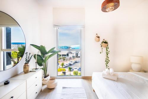 a white bedroom with a mirror and a large window at Voyage's Stylish 1br At Waters Edge in Abu Dhabi