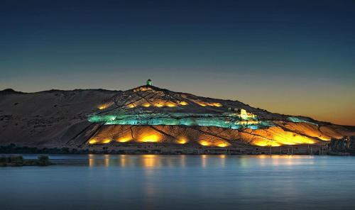 a mountain with lights on it next to a body of water at برنامج سياحي كامل داخل اسوان in Aswân Reservoir Colony