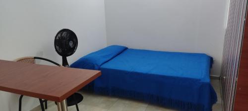 Schlafzimmer mit einem Bett mit blauer Tagesdecke und einem Tisch in der Unterkunft Apartaestudio cerca al parque principal in Los Andes