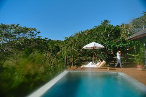 Bumbang的住宿－TUNAK Resort Lombok，两人坐在游泳池旁的伞下