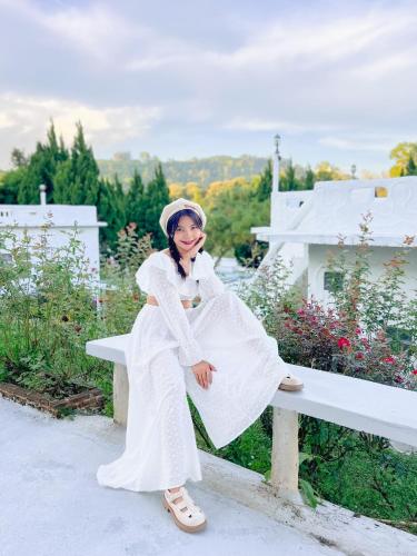 a woman in a white dress sitting on a bench at เนริสารีสอร์ท เขาค้อ in Ban Khao Ya Nua