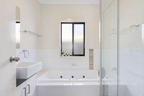 ein weißes Badezimmer mit einer Badewanne, einem Waschbecken und einem Spiegel in der Unterkunft Calm Waters in Port Moonta