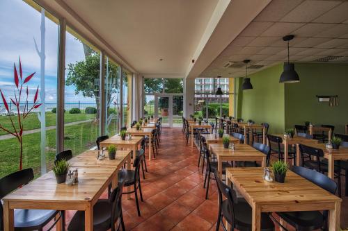 a restaurant with wooden tables and chairs and large windows at Hotel Lido in Siófok