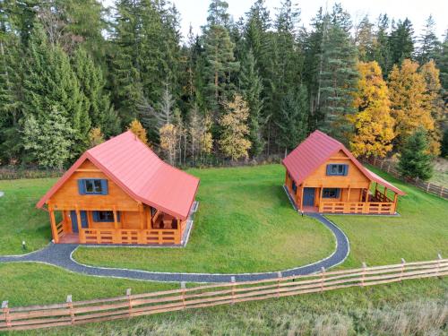 two log homes with red roofs on a green field at Okno na las in Polanica-Zdrój