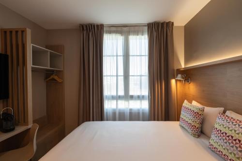 a bedroom with a white bed with a window at Campanile Caen Centre Gare in Caen