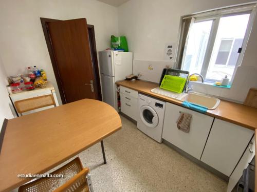 a kitchen with a table and a sink and a washing machine at EEM Only Girls Student Residence in Is-Swieqi