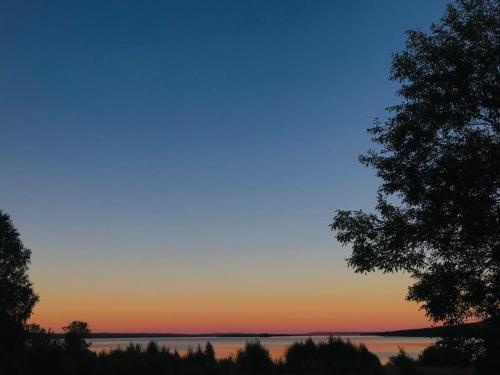 a sunset over a lake with a tree in the foreground at Gästhuset Gubbhögen in Strömsund