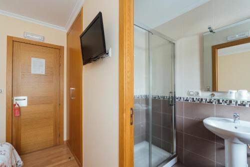 TV y baño con ducha y lavabo. en Hotel Restaurante Cazador en Pereiro