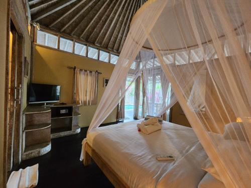 a bedroom with a white canopy bed with a television at Bamboo Lodge in Gili Trawangan