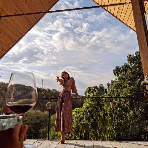 a woman standing on a balcony holding a glass of wine at Cottage Sataplia in Kutaisi