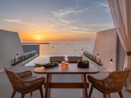 a table on a balcony with a view of the ocean at Santo Mine Oia Suites in Oia