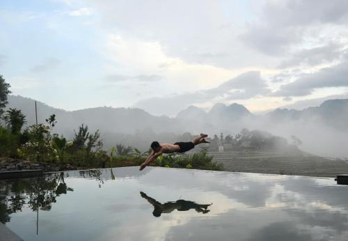 a person diving into a pool of water with mountains in the background at Inh La Home Pu Luong in Pu Luong