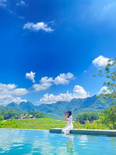 a woman sitting in a pool of water taking a picture of mountains at Inh La Home Pu Luong in Pu Luong