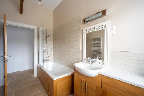 a bathroom with a sink and a tub and a mirror at Filby Barn by Big Skies Cottages in Docking