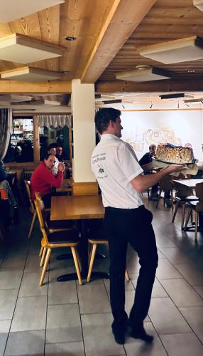 a man standing at a table holding a pizza at Hameau des Prodains - Hôtel in Morzine