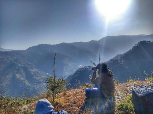 a person sitting on a hill taking a picture of the mountains at Vintage Woods Inn in Shimla