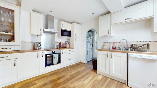 cocina blanca con suelo de madera y armarios blancos en Charming 2-Bedroom Flat in the Heart of Cro London ER1 en South Norwood
