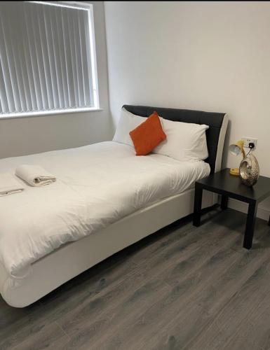 Cama blanca con almohada naranja y mesa en ASM London Road Studio Apartments, en Leicester