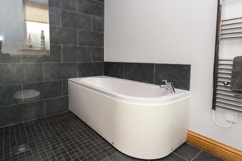 a white bath tub in a bathroom with black tiles at Galloway View in Castle Douglas