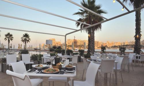a restaurant with white tables and chairs and a view of the city at Cavalieri Art Hotel in St. Julianʼs