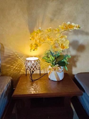 a table with a lamp and a vase with yellow flowers at Smilingface guesthouse in Sukhothai