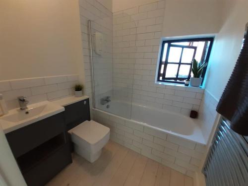 ein Badezimmer mit einem Waschbecken, einem WC und einer Badewanne in der Unterkunft Light & Airy Vaulted Barn Conversion with a View in Sampford Arundel