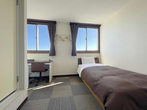 a bedroom with a bed and a desk and windows at 釜石駅から徒歩5分ホテルマルエHotelMarue in Kamaishi