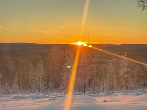 a sun setting over a snow covered field with the sun shining at Tunnelmallinen ja ihana mökki in Rovaniemi