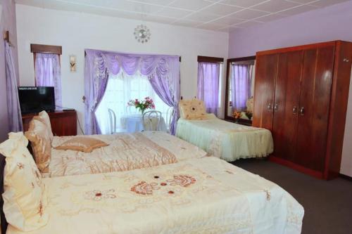 1 dormitorio con 2 camas y una ventana con cortinas moradas en Heavenly Home Inn, en Nuwara Eliya