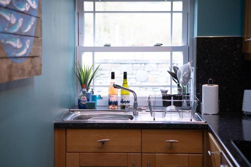 a kitchen sink with bottles of wine and a window at Vineyard Country Cottage in Llanerch-Aeron