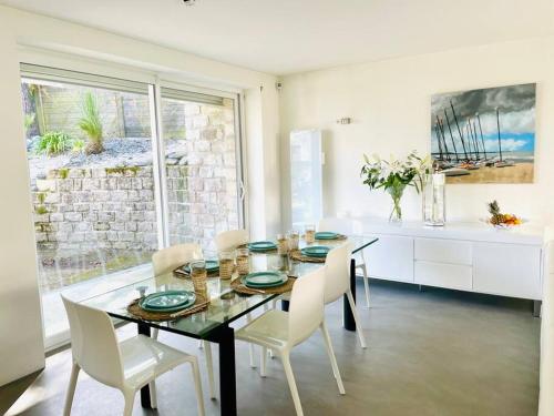 une salle à manger avec une table en verre et des chaises blanches dans l'établissement Villa Les Sorbiers, à La Baule