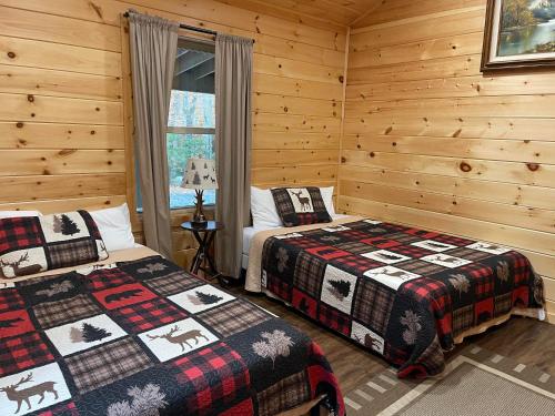 two beds in a room with wooden walls at Camp Adirondack in Eagle Bay
