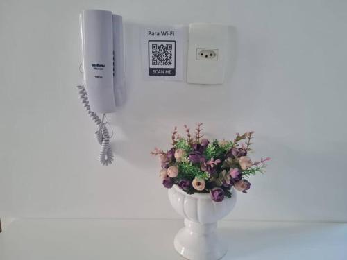 a white vase with a bouquet of flowers next to a phone at Apart hotel Tagualife in Riacho Fundo