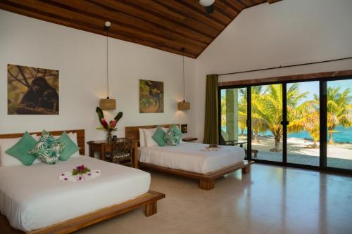 two beds in a room with a view of the ocean at Little Harvest Caye - Your Own Private Island in Placencia