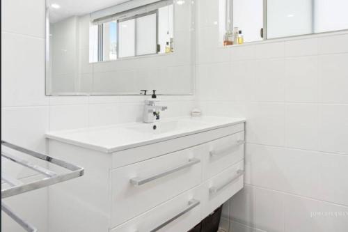 a white bathroom with a sink and a mirror at Absolute Hastings Street Noosa Suite in Noosa Heads