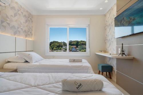 una camera d'albergo con tre letti e una finestra di Apartamento HodsPrime com 2 Suítes by Achei a Canela