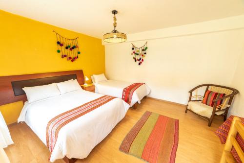 two beds in a room with yellow walls and a chair at Hospedaje Chaska Pisac in Pisac