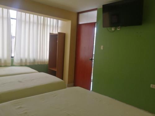 a room with two beds and a door with a television at Hostal Boulevard in Nazca