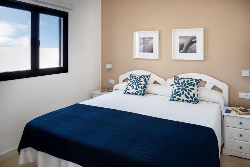 ein Schlafzimmer mit einem großen weißen Bett mit blauen Kissen in der Unterkunft Delmar Natur - Sama in Charco del Palo