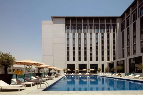 a pool with chairs and umbrellas in front of a building at Rove At The Park in Dubai