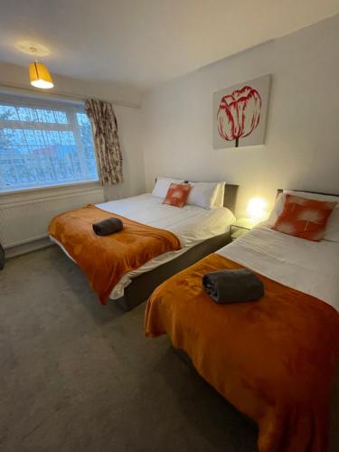 a bedroom with two beds with orange sheets and a window at Wardown Place - Spacious 3 Bed House available for short term or long term Rental in Luton