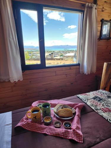 a table with a tray of food on a bed with a window at Cabañas Alechen in El Calafate